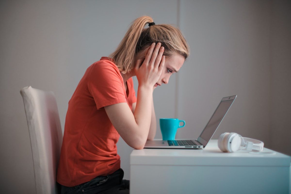 nő fejét fogva ül a laptop előtt, a monitorra bámulva