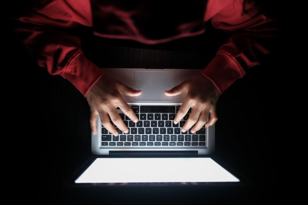 sötét háttér előtt világos monitor előtt ül egy pirps pulcsis ember felülről fotózva